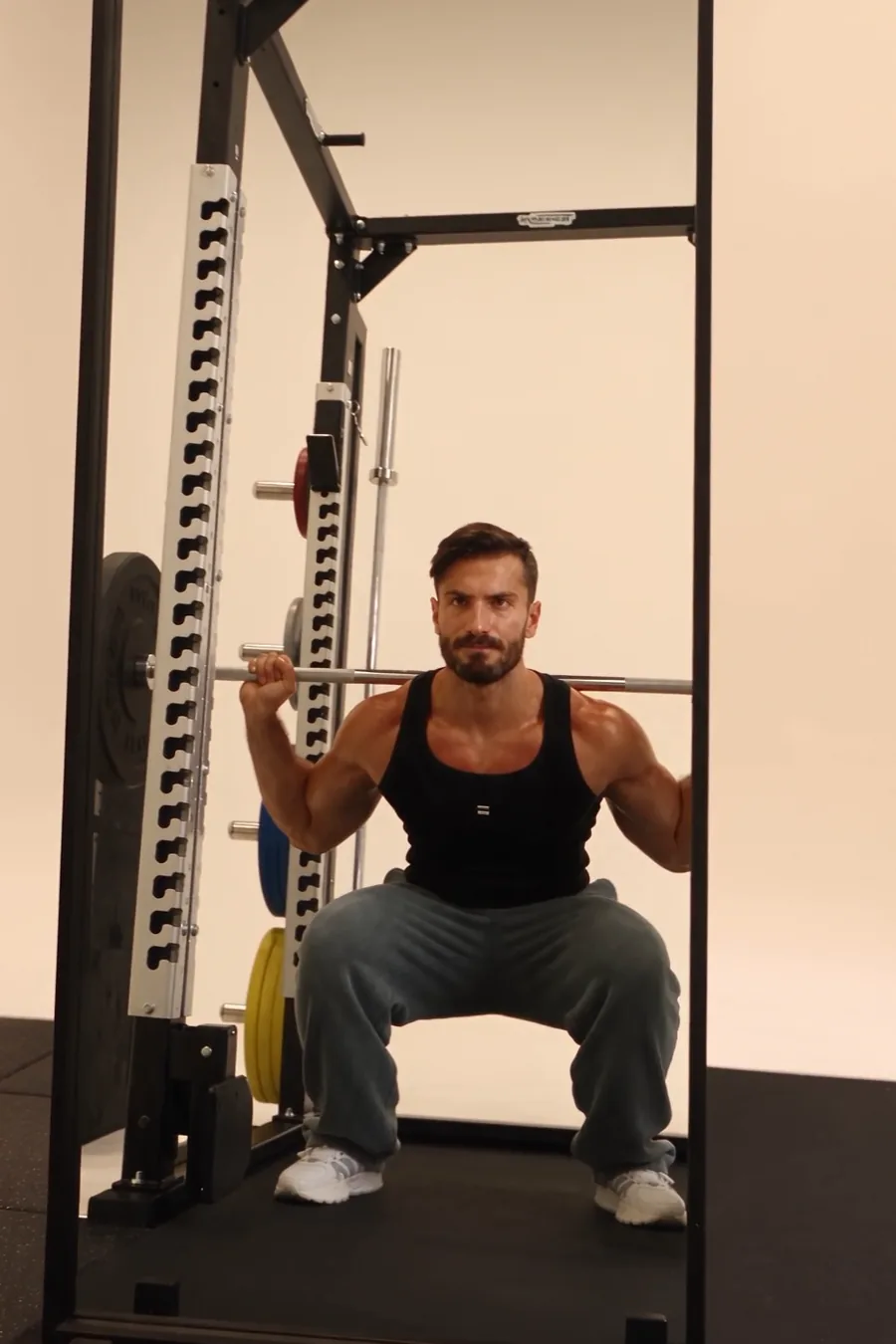 A lifter at the bottom of a barbell back squat, square on to a full-length mirror that shows only his reflection.